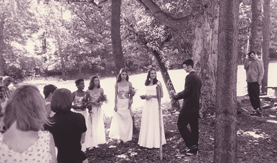 Alex and Nate's wedding ceremony in sepia tone. Alex's bridesmaid stand beside her outside surrounded by trees
