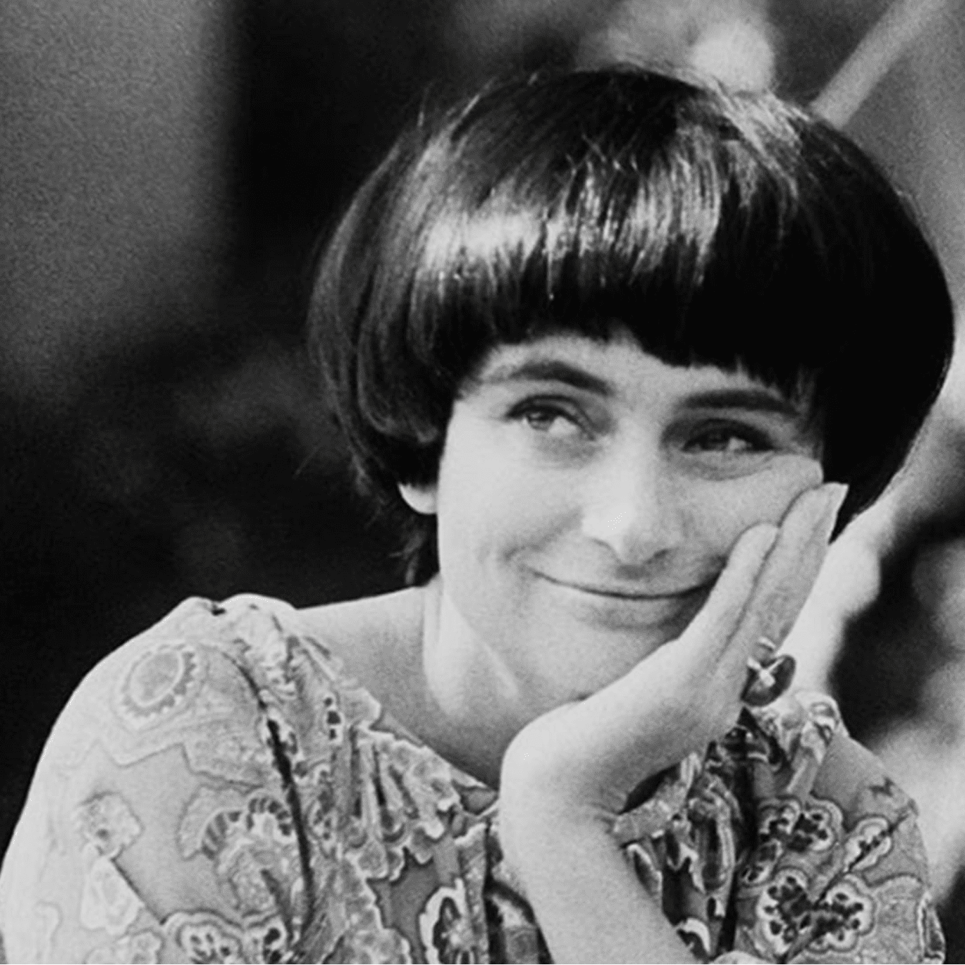 A young Agnès Varda smiles to the side, her hand resting on her chin, in a black and white photo.