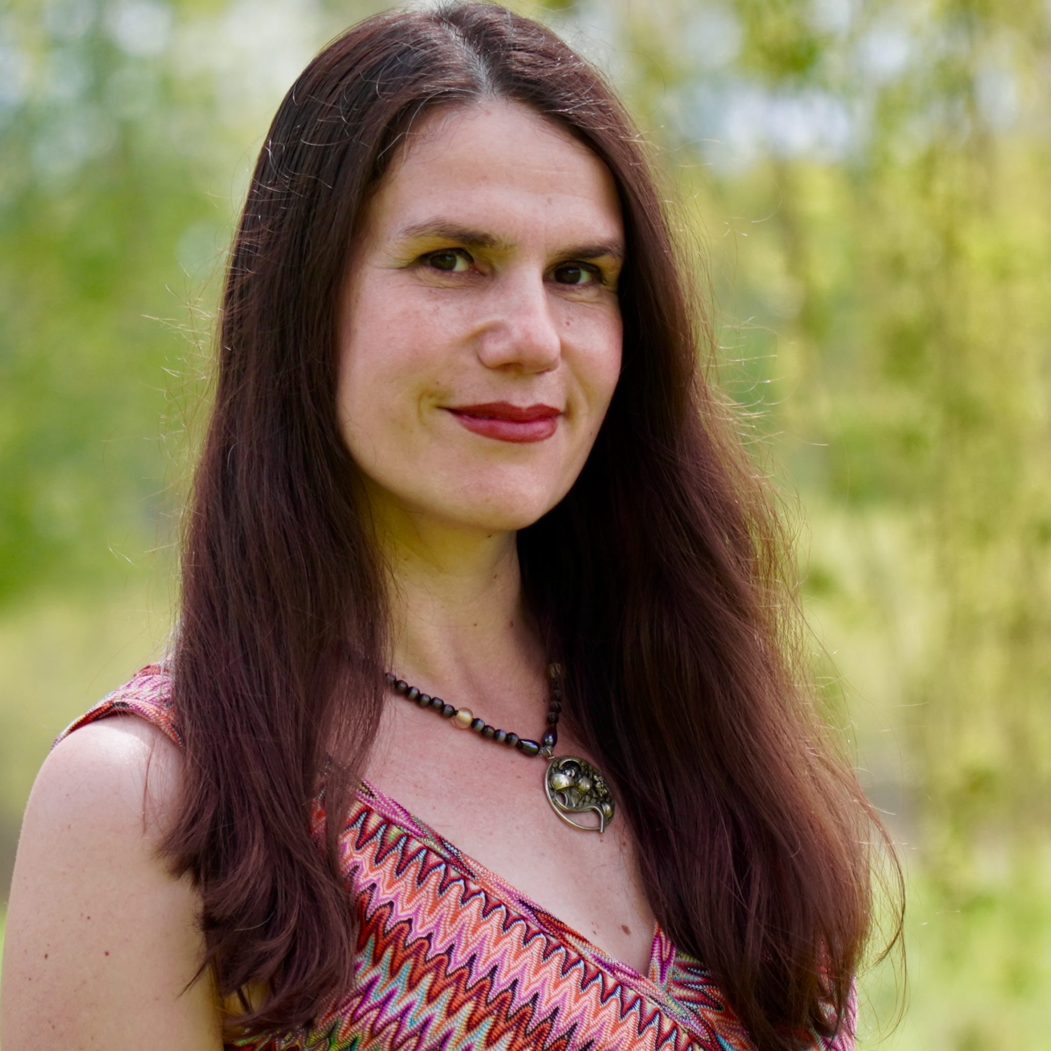 Alexandra faces the camera and smiles. She is wearing a patterned pink dress with a silver necklace